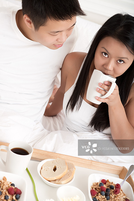 一对亚洲年轻夫妇在床上吃早餐图片素材