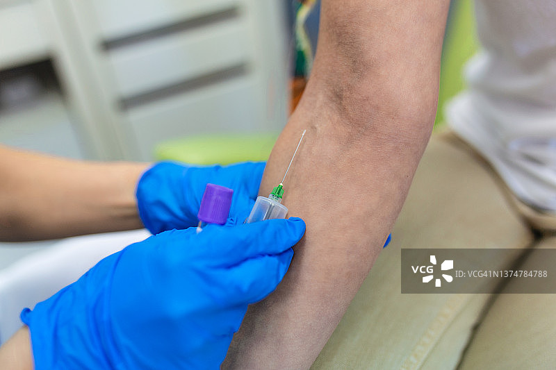 医疗技术人员为病人抽血服务。实验室助理带着无菌橡胶手套从病人身上采集血样。图片素材