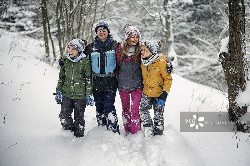 快乐的家庭徒步旅行在美丽的冬季森林图片素材
