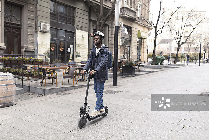 一个非洲裔美国年轻人骑着他的滑板车在城市里穿行图片素材