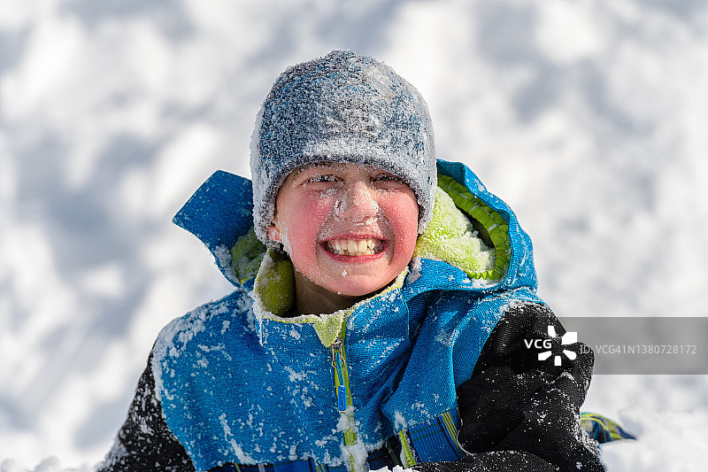 脸上被雪覆盖的微笑男孩在雪中玩耍图片素材