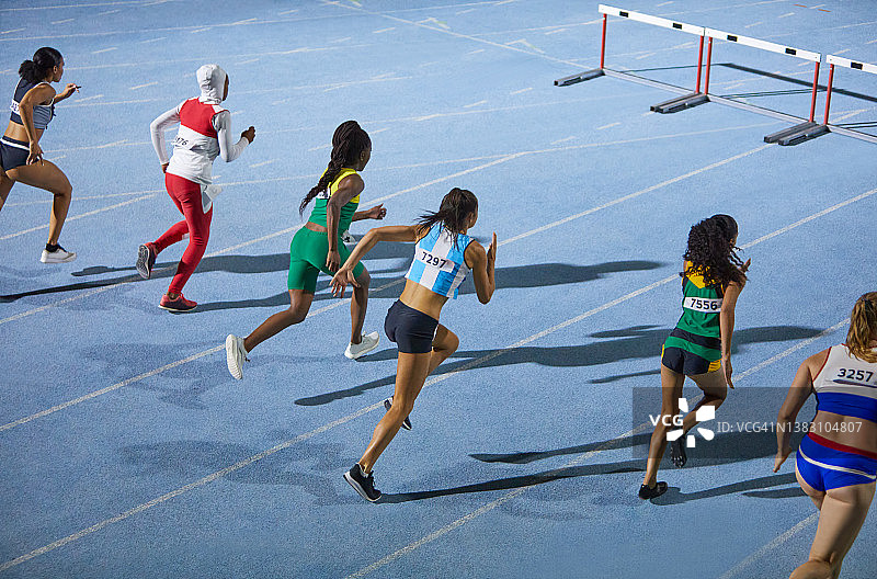 女子田径运动员在蓝色跑道上进行跨栏比赛图片素材