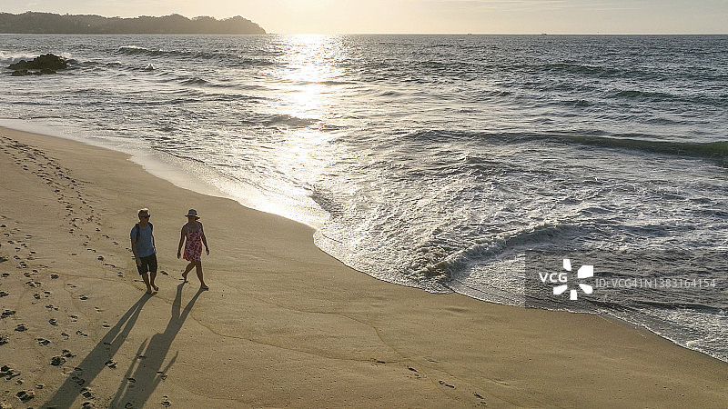鸟瞰图，情侣在日出时沿着海滩散步图片素材