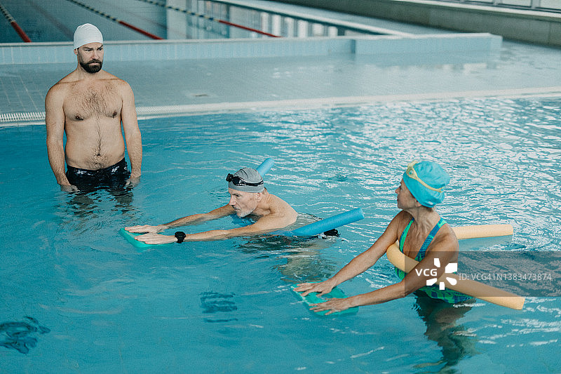 教练协助高级男女在游泳池游泳图片素材