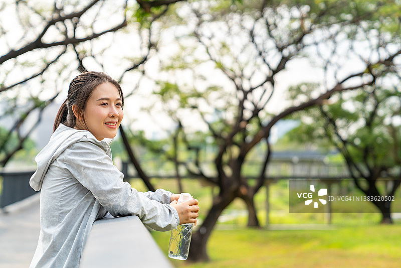 亚洲妇女在公园晨跑时喝瓶装水。图片素材