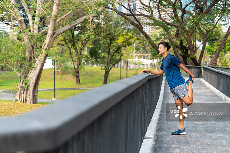 亚洲男子伸展身体，而慢跑运动在公园早上。图片素材