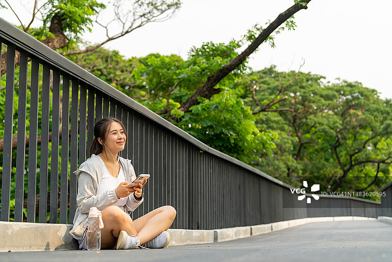 亚洲妇女听音乐，而慢跑在公园早上。图片素材
