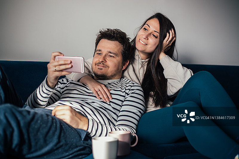 情侣坐在沙发上，用智能手机看视频图片素材