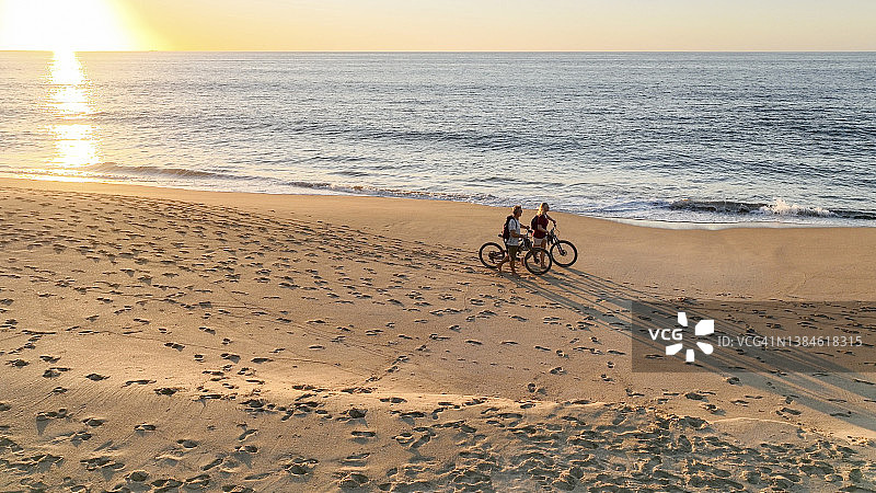 一对夫妇在沙滩上推着自行车的鸟瞰图图片素材