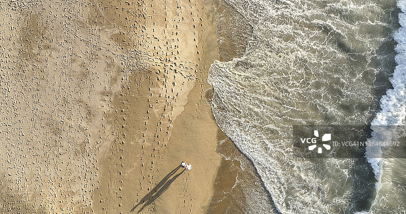 鸟瞰图，一对夫妇在日出时沿着海滩散步图片素材