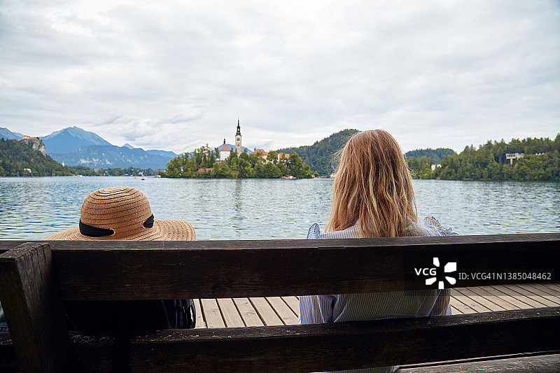 年轻的成年旅游妇女坐在长椅上享受湖。图片素材