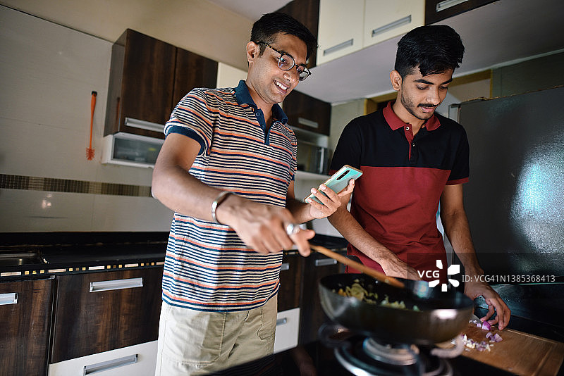 一个中年男子和一个十几岁的男孩在厨房里一起烹饪食谱图片素材