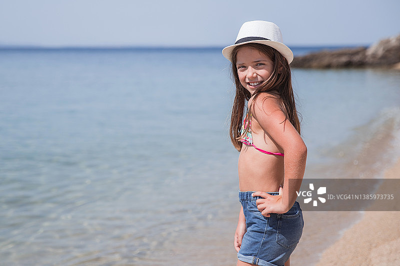 快乐的女孩与她的手在她的臀部看着相机在海滩上图片素材