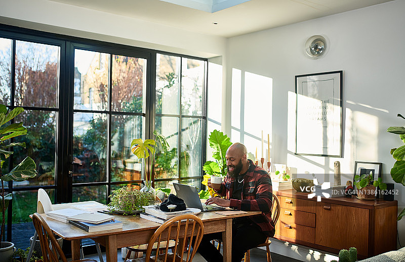 黑人企业家在家庭办公室喝咖啡，在笔记本电脑上轻松地开会图片素材