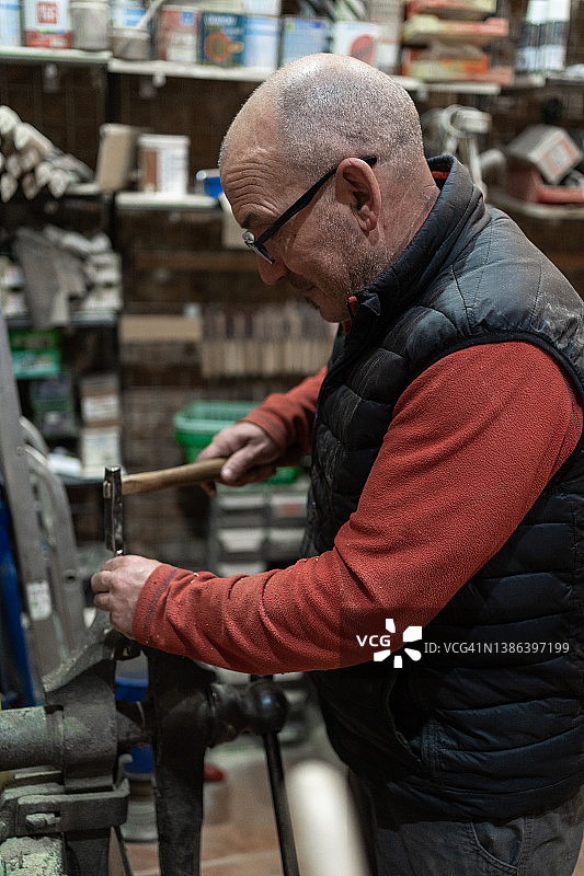一个中年木匠在他杂乱的车间里用液压千斤顶和一把工艺刀的手柄工作图片素材