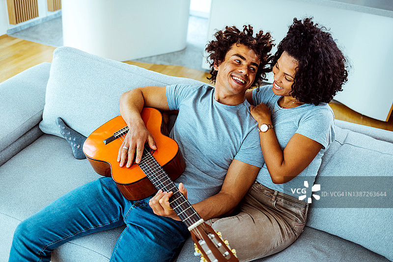 幸福的夫妇在家里的沙发上一起唱歌和弹吉他图片素材