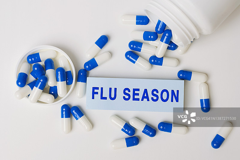 流感季节——从药瓶中溢出的蓝白色药丸旁边的纸条上写着这句话。医学的概念图片素材