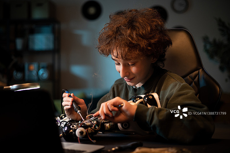 一个卷发的孩子坐在桌子旁，忙着焊接机器人、修理电线、电缆、玩具电子产品图片素材
