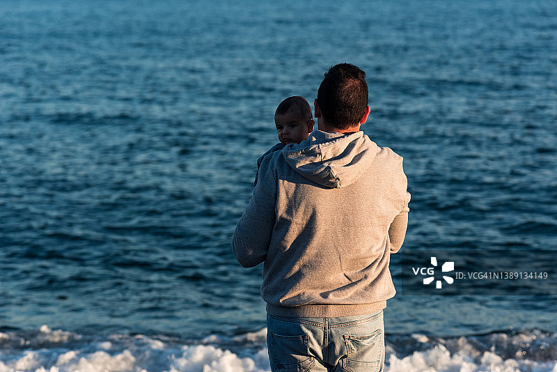 父亲抱着孩子凝视大海。图片素材