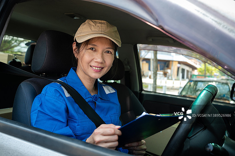 一名身穿蓝色制服、头戴棒球帽的女快递员坐在驾驶座上检查客户的送货地址图片素材