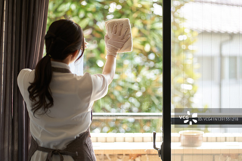 一个亚洲女人在擦客厅的窗户图片素材