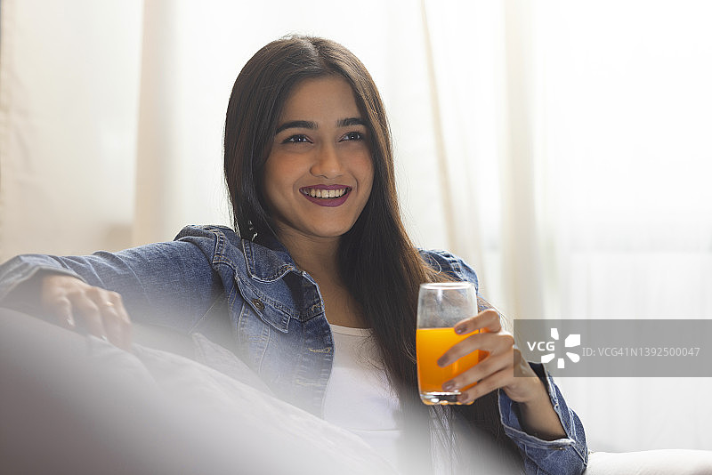 拿着一杯果汁的年轻女孩微笑着望向别处图片素材