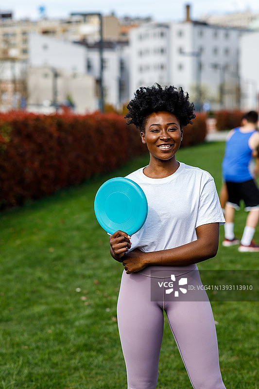 一名非裔美国妇女站在公园里，手里拿着飞盘。图片素材