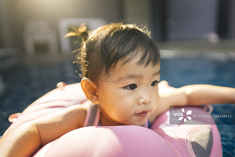 积极的情感亚洲女婴戴着浮动的戒指，供婴儿在游泳池里玩耍图片素材