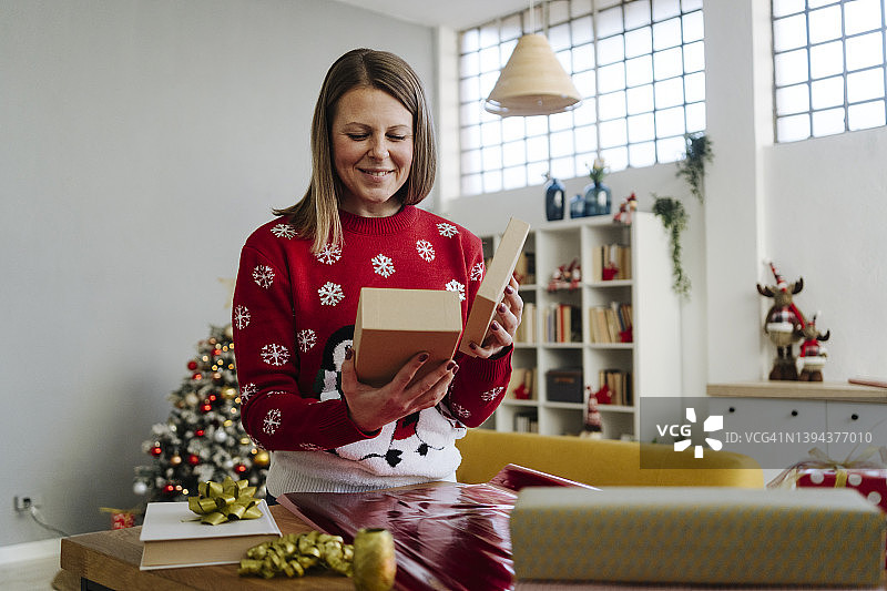 微笑的女人看着礼物盒在客厅图片素材