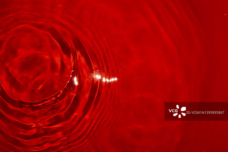 平静的红色水和水滴形成的戒指在左边角落的抽象水的背景，浪漫的夏天设计图片素材