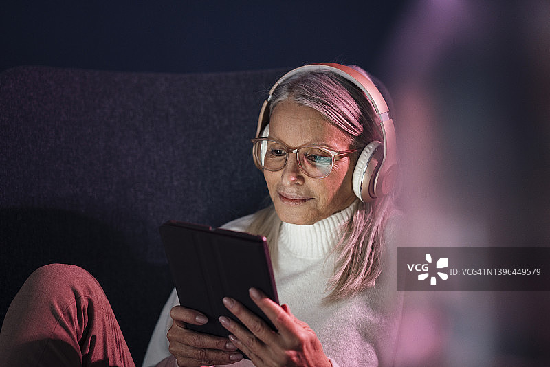 老妇人戴着耳机，坐在椅子上使用平板电脑图片素材
