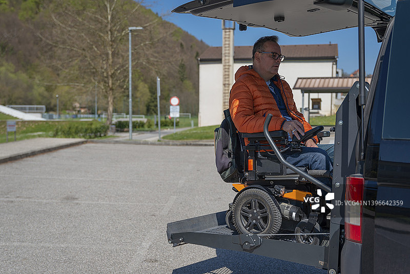 一名坐电动轮椅的残疾人乘坐电动电梯进入一辆面包车。在车的前面，在车上。图片素材