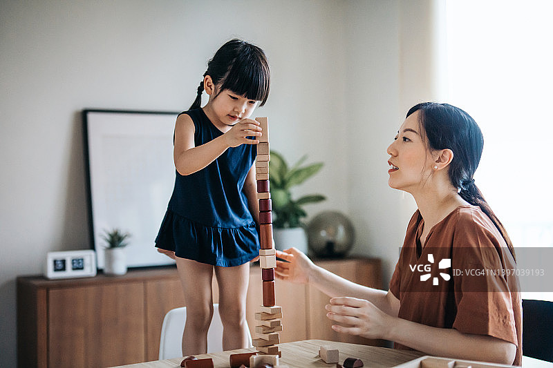年轻的亚洲母亲和小女儿玩木制积木在一起，享受母亲和女儿在家里的纽带时间图片素材