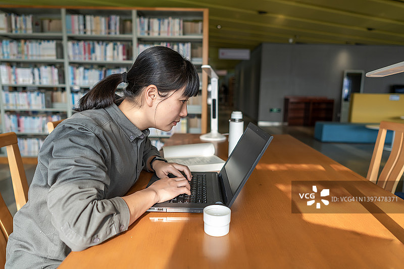 一位亚洲女学生在书店的阅读区用笔记本电脑学习图片素材