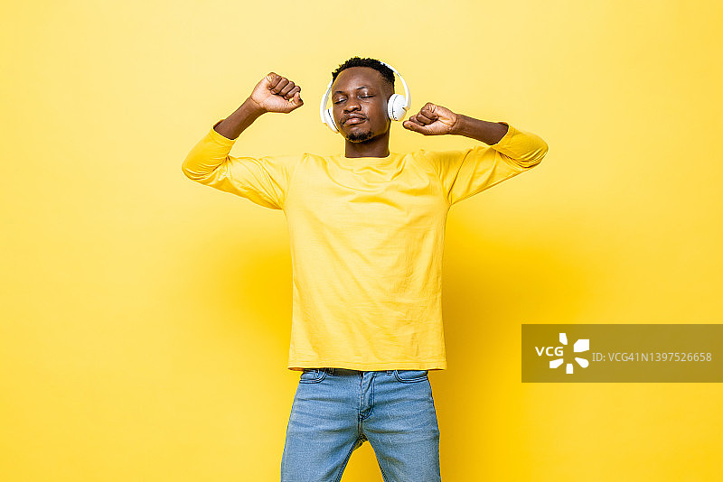 肖像的年轻非洲人听音乐耳机上闭上眼睛和舞蹈对黄色的工作室背景图片素材