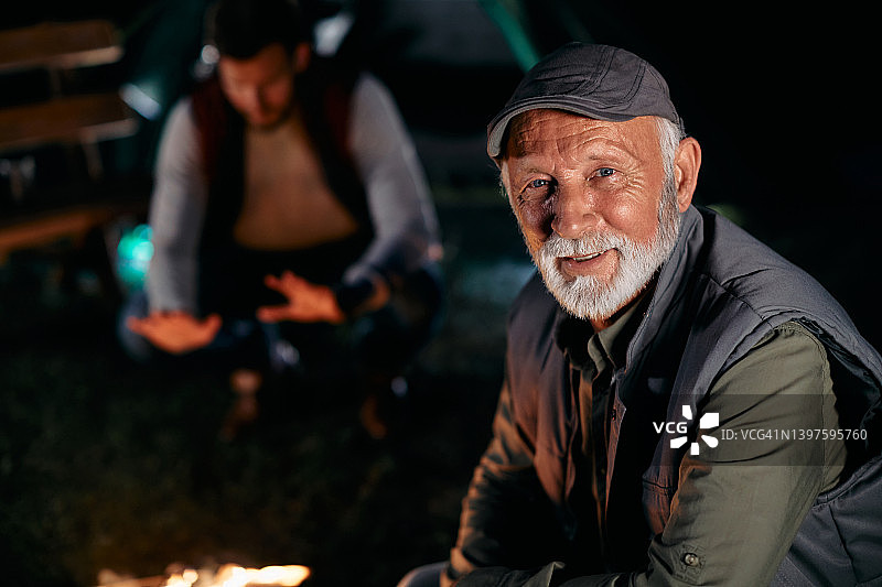 老人喜欢晚上和儿子一起露营，看着镜头。图片素材