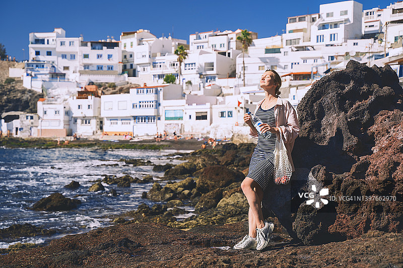 时髦的女人与水果在海滩棉袋，加那利群岛，西班牙。快乐的年轻女孩旅游放松，享受野餐在小村庄的假期。低浪费，生态旅游，地方旅游。图片素材