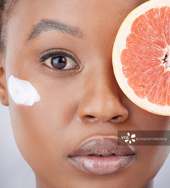 工作室拍摄了一个迷人的年轻女子拿着一个切片葡萄柚，并在她的脸上涂抹润肤霜图片素材