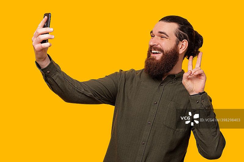大胡子男子用手机自拍时摆出了“V”手势。图片素材