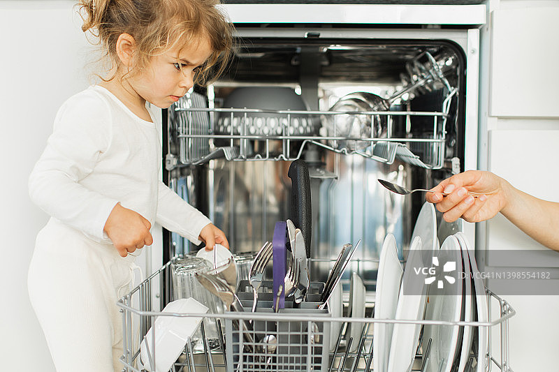 孩子把脏餐具放进家里的洗碗机。图片素材