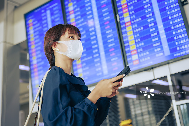 年轻的亚洲女企业家们戴着口罩，在机场登机牌前阅读电子邮件。商务旅行的概念。图片素材