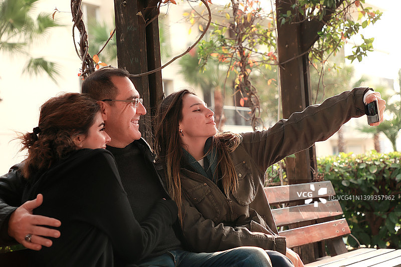 父亲和年轻的成年女儿在公园用智能手机自拍图片素材