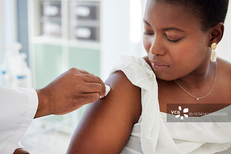 一位非洲裔美国病人正在看医生清洗她的手臂。全科医生用棉签清洁病人手臂的手。医生在注射前擦拭病人的手臂。图片素材