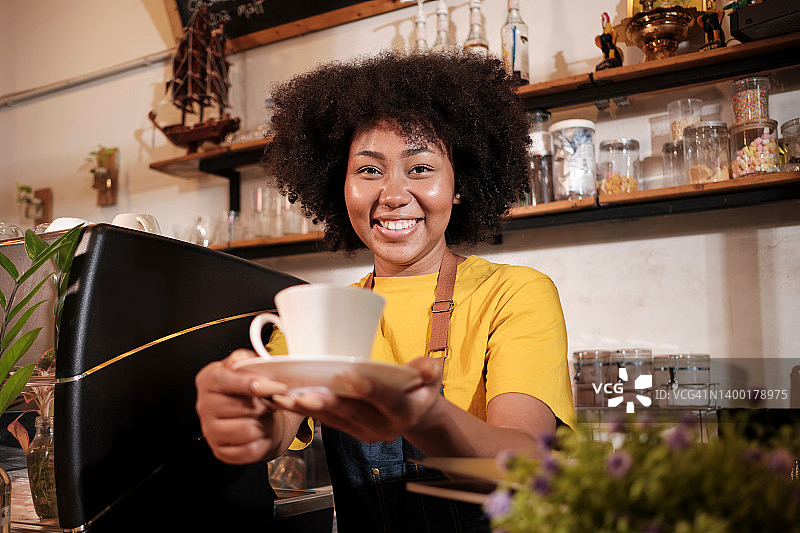 非裔美国女咖啡师在休闲咖啡馆愉快地提供一杯咖啡。图片素材