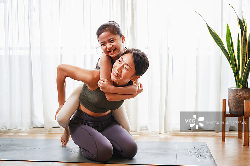 亚洲年轻母亲教她的女儿瑜伽姿势和锻炼一起在瑜伽垫上图片素材