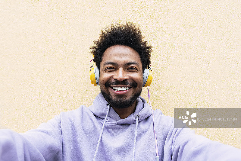 微笑的男子在奶油色的墙前戴着耳机听音乐自拍图片素材