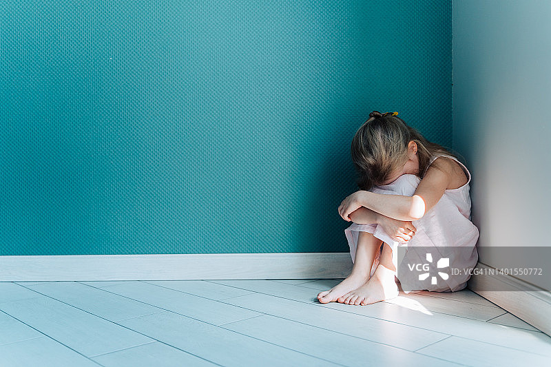 一个有点悲伤和沮丧的金发女孩穿着白裙子坐在室内角落的地板上图片素材