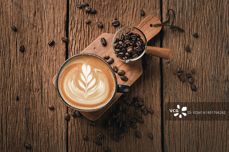 热拿铁咖啡上的拉花艺术。香气咖啡杯和咖啡豆放在木桌上。图片素材