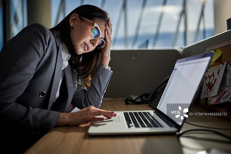 年轻的女商人在办公室用笔记本电脑工作时头痛。图片素材