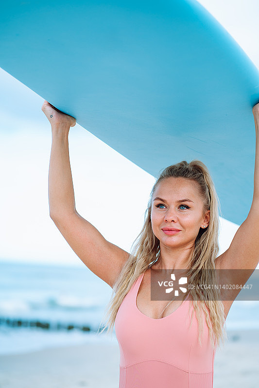 快乐的女冲浪者带着蓝色的冲浪板在海面上图片素材